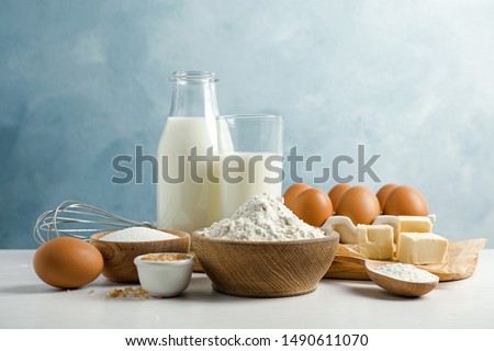 Fresh ingredients for delicious homemade cake on white wooden table against blue background