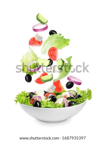 Fresh ingredients for Greek salad falling into bowl on white background