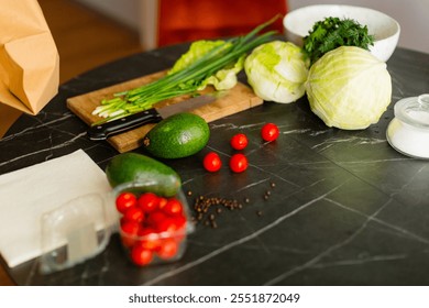 Fresh ingredients, including avocado, lettuce, cherry tomatoes, and green herbs, neatly arranged on a wooden cutting board with a kitchen knife.
A composition of vegetables on a dark marble countertop - Powered by Shutterstock