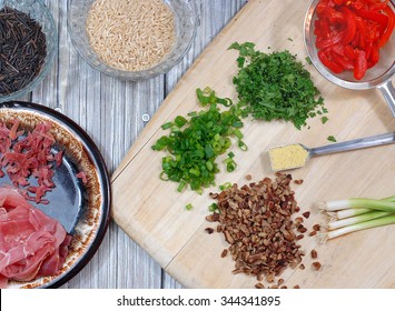 Fresh Ingredients Of A Wild Rice And Brown Rice Dressing Recipe Also Includes Prosciutto, Pecans, Green Onions, Parsley And Pimento. The Ingredients Are Scattered On A Wood Table Top And Cutting Board