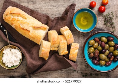 Fresh Italian baguette cut in slices on wooden table with oil, olives, garlic, herbs, goat cheese and cherry tomatoes, top view. Ingredients for making bruschetta - Powered by Shutterstock