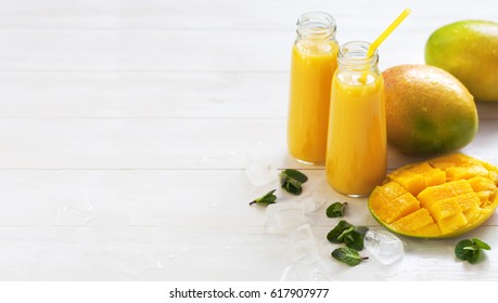 Fresh juice of a mango smoothies in a glass bottle and ripe mango fruit on a white wooden background.