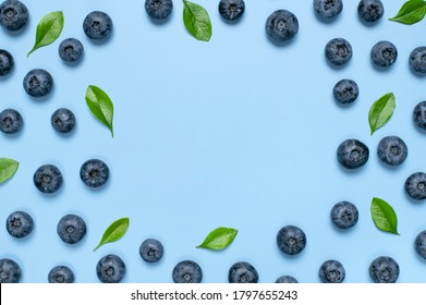 Fresh juicy blueberries with green leaves on blue background. Blueberries background. Flat lay top view copy space. Healthy berry, organic food, antioxidant, vitamin, blue food. Blueberry frame