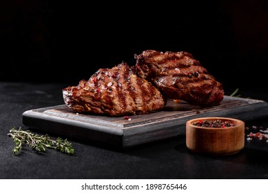 Fresh juicy delicious beef steak on a dark background. Meat dish with spices and herbs - Shutterstock ID 1898765446