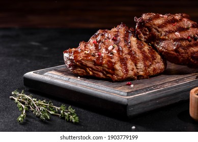 Fresh juicy delicious beef steak on a dark background. Meat dish with spices and herbs