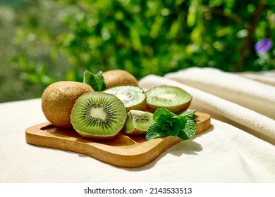 Fresh juicy kiwi and green mint leaves in plate on the table with linen tablecloth in the garden. Sliced ripe exotic fruits. Space for text. - Powered by Shutterstock