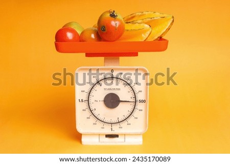 Fresh and juicy star fruits and tomatoes on weighing scale isolated on yellow color background