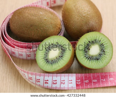 Fresh kiwi fruit and tape measure on wooden table. Diet concept.