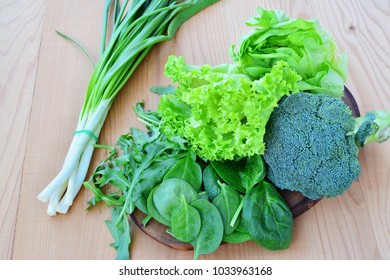 Fresh leafy vegetables, broccoli, lettuce, arugula, salad, spinach, scallions on wooden table