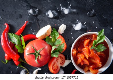 fresh Lecho  with a sprig of green parsley, herbs, tomato slices, red chili pepper, garlic, ice cubes, on a black background, sauce top view, - Powered by Shutterstock