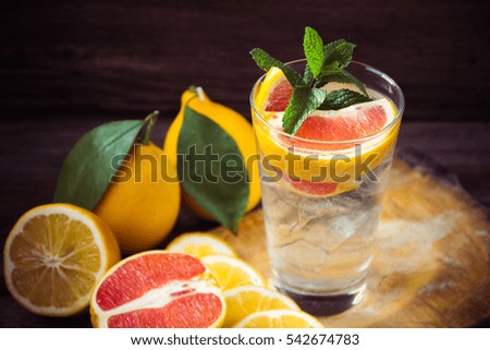 Fresh lemonade in a glass beaker with ice, green mint, red orange and lemon on the wooden background
