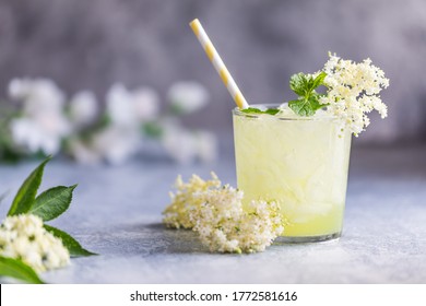 Fresh lemonade with lemon, lime juice and elderberry flowers. Healthy organic homemade refreshing nonalcoholic lemonade mocktail made of elderflower cordial juice. With a paper straw. Gray background.