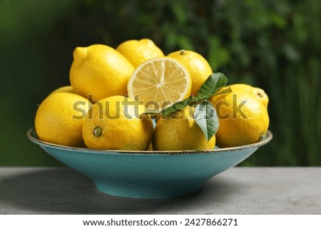 Fresh lemons and green leaves on grey table outdoors