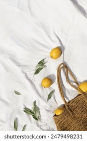 Fresh lemons, wicker bag and cute olive twigs on the white sheet on the beach. Flat lay, top view, healthy organic concept
