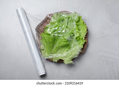 Fresh Lettuce With Plastic Food Wrap On Light Grey Table, Flat Lay