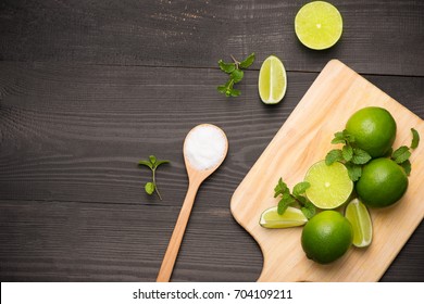 Fresh Limes On Cutting Board On Wooden Table With Spoon Of Salt. Top View, Background.