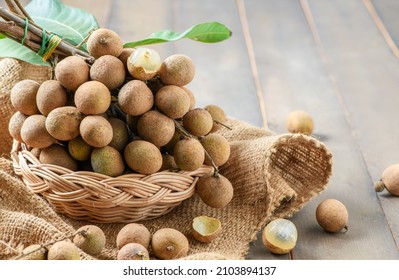 Fresh longan fruit with leaves in bamboo basket on wood background, Asia fruit