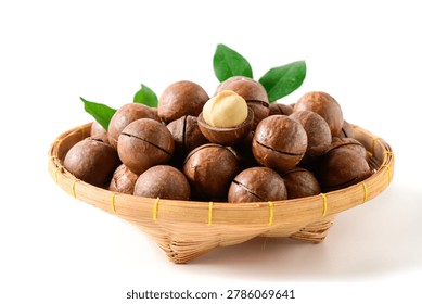 Fresh macadamia nuts in shells displayed in a bamboo basket with green leaves on a white background. Healthy organic food concept featuring premium nuts rich in nutrition and natural flavor.