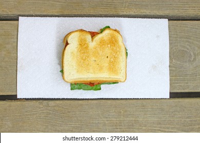 A Fresh Made Bacon Lettuce And Tomato Sandwich Served On A Paper Towel On Top Of An Old Wooden Picnic Table Outside During The Summer