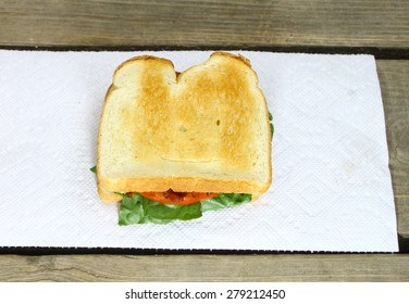 A Fresh Made Bacon Lettuce And Tomato Sandwich Served On A Paper Towel On Top Of An Old Wooden Picnic Table Outside During The Summer