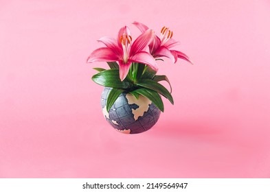 Fresh magenta lillies growing from a globe against pastel pink background. Earth day creative concept. Artistic design for wallpaper or card or editorial