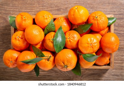 Fresh mandarin oranges fruit or tangerines with leaves in a wooden box, top view