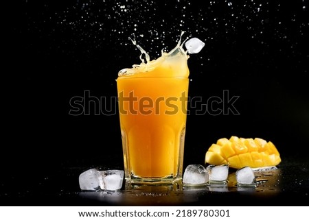 Fresh mango juice. A splash of mango cocktail on a black background. Ice cubes fall into the mango juice
