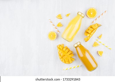 Des jus frais de mangue et d'orange dans des bouteilles en verre avec des fruits coupés, pailles sur planche en bois blanc, vue supérieure, espace de copie, modèle pour le design, publicité, portfolio.
