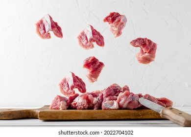 Fresh Meat Levitation. Chopped Pieces Of Pork Lie On A Cutting Board With A Knife On A White Plate. Cooking, Cutting Meat.