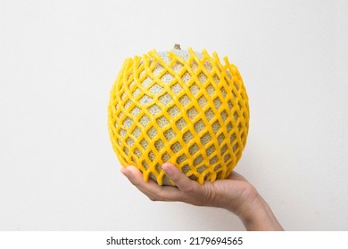 Fresh Melon covered by Shockproof foam yellow with hand hold up . Japanese melons, honey melon or cantaloupe with foam net. Green melon or cantaloupe in fruit packaging net. On cream color background. - Shutterstock ID 2179694565