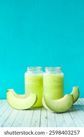 Zumo de melón fresco en un vaso decorado con rodajas de melón fresco en el lado, dos vasos de melón fresco en un vaso con un fondo azul vibrante