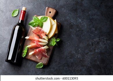Fresh melon with prosciutto and basil. Antipasti and red wine bottle. Top view on dark stone table with copy space for your text - Powered by Shutterstock