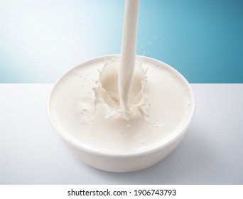 Fresh Milk Pouring In Bowl With Splash. Isolated On Blue And White Background.