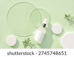 Fresh mint green background featuring serum dropper bottle and glass transparent discs, cream jars and sprig of rosemary. Spa concept. Top view with space for text