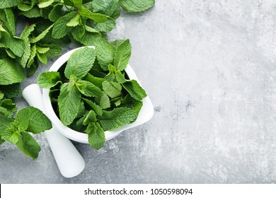 Fresh mint leafs in mortar on grey wooden table