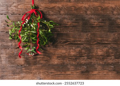 Fresh mistletoe branches with red ribbon bow hanging on wooden background with blank space for text. Natural Christmas decor concept. - Powered by Shutterstock