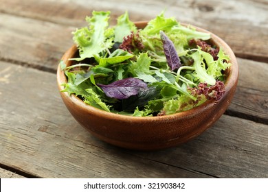 Fresh mixed green salad in bowl on wooden table close up