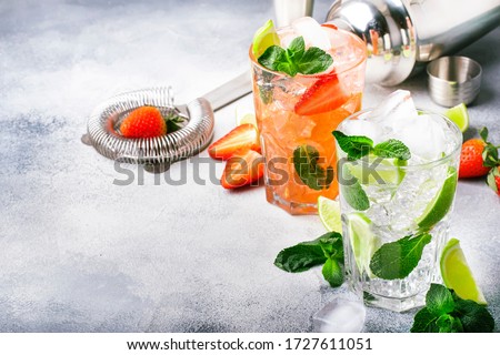 Fresh Mojito cocktail set with lime, mint, strawberry and ice in glass on gray background. Summer cold alcoholic non-alcoholic drinks, beverages and cocktails. Steel bar tools. Copy space