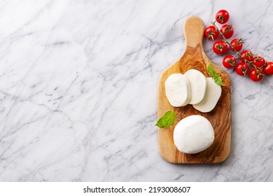 Fresh mozzarella cheese with cherry tomatoes on cutting board. Marble background. Copy space. Top view.