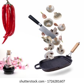 Fresh Mushrooms Falling Into A Frying Pan, A Bottle Of Soy Sauce, And A Bunch Of Chilli On A White Isolated Background