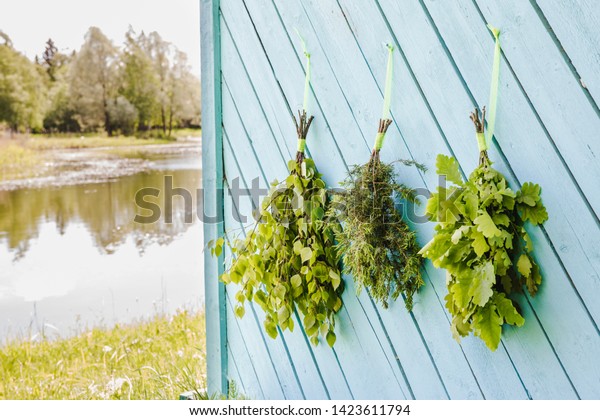 Fresh oak, birch, juniper and oak\
tree sauna whisks brooms hanging and drying on sauna house wall by\
beautiful natural lake. Traditional Finnish sauna\
concept.