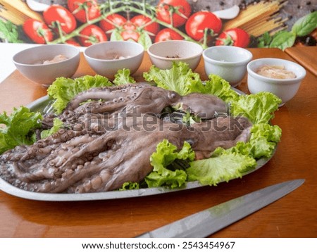 Fresh octopus presented on a bed of lettuce, accompanied by a selection of dipping sauces, perfect for gourmet seafood preparation.
