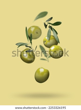 Fresh olives and leaves falling on pale yellow background