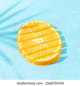 Fresh orange fruit slices with palm leaf shadow on bright blue wet background. Minimal food concept. Creative summer vacation aesthetic. Trendy refreshment idea.
