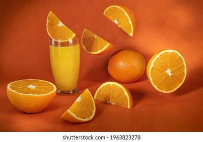 Fresh Orange Juice In Glass And  Falling Slices Of Orange Fruit.Orange Background.Monochromatic Food Photography.