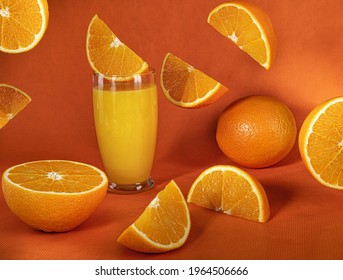 Fresh Orange Juice In Glass And  Falling Slices Of Orange Fruit.Orange Background.Monochromatic Food Photography.