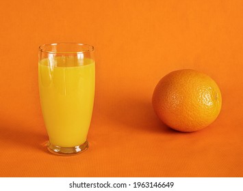 Fresh Orange Juice In Glass And One Whole Orange  On A Orange Background.Monochromatic Food Photography.Copy Space.