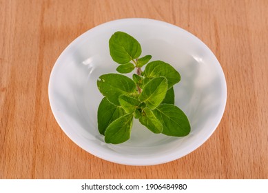 Fresh Oregano sprig in a small white bowl placed on a kitchen wooden chopping board