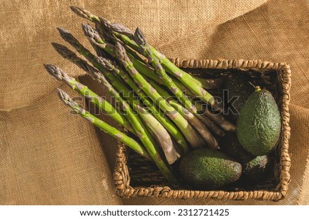 Fresh organic asparagus and avocados in a whicker basket close-up on rustic background, view from above
