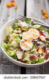 Fresh organic Cobb salad topped with homemade Ranch dressing, hard boiled eggs, bacon, peppers, peas, and green onions on an old weathered barn wood table